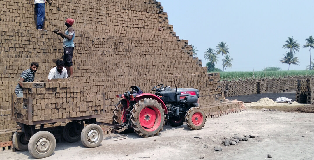 This image shows the brick kiln after mechanization. Workers are stacking a brick tower using bricks from a trolley attached to a tractor.