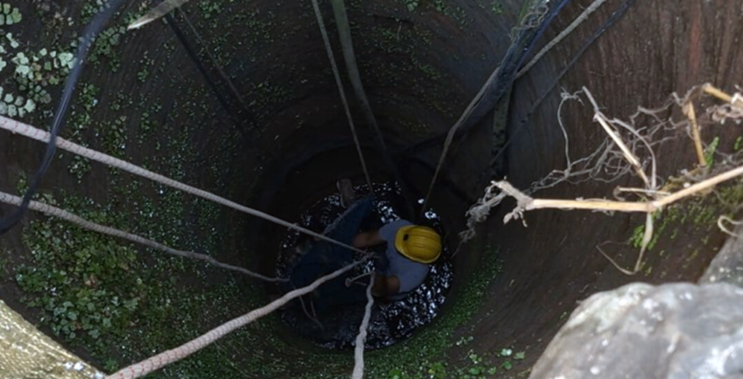 The image shows an Animal Rahat rescuer in a deep well, rescuing a dog.